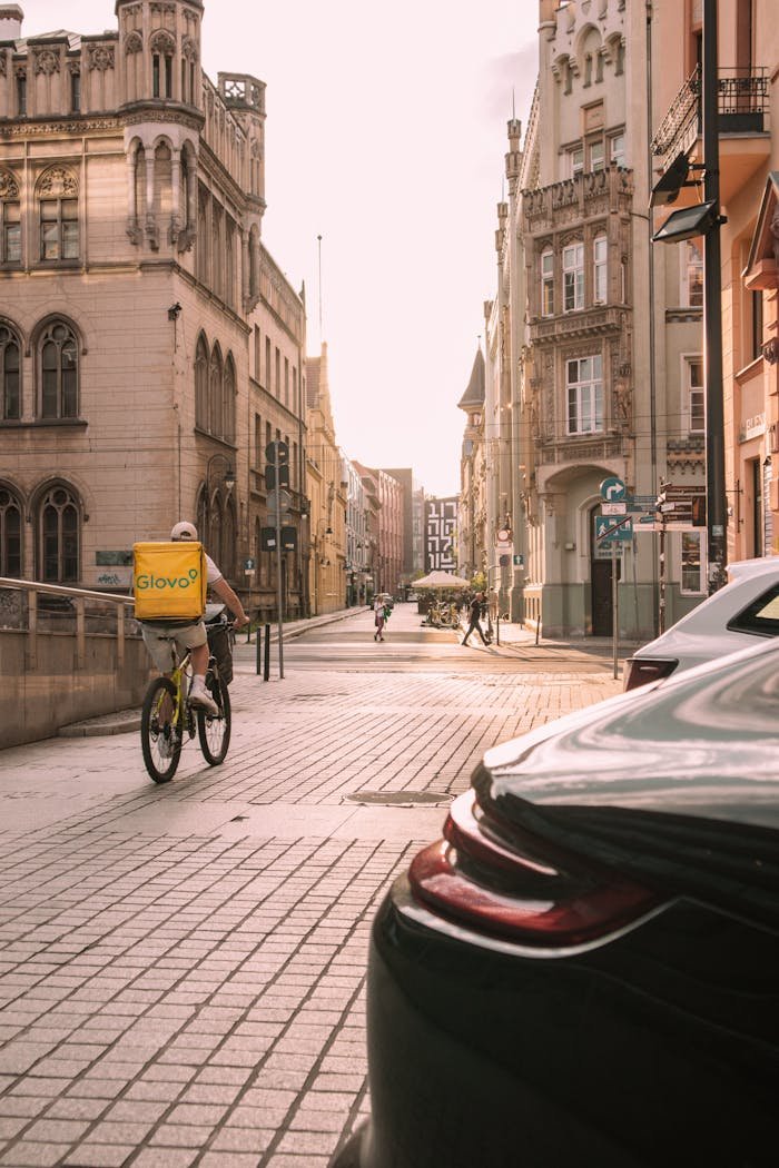 Bicycle courier rides through a sunlit street in Wrocław, Poland, capturing urban life.
